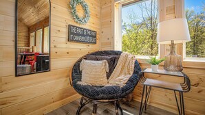 Une pièce chaleureuse avec un fauteuil rond, un miroir, une table avec une lampe et un panneau accroché au mur.