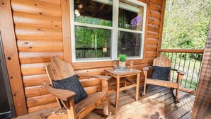 Une cabane en bois dotée d’une véranda, de deux fauteuils Adirondack, d’une petite table et d’une fenêtre donnant sur un paysage verdoyant.