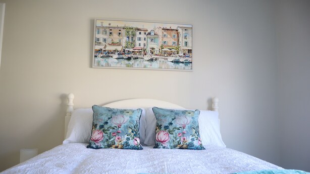 A bed with a white headboard, two floral pillows, and a teal blanket.