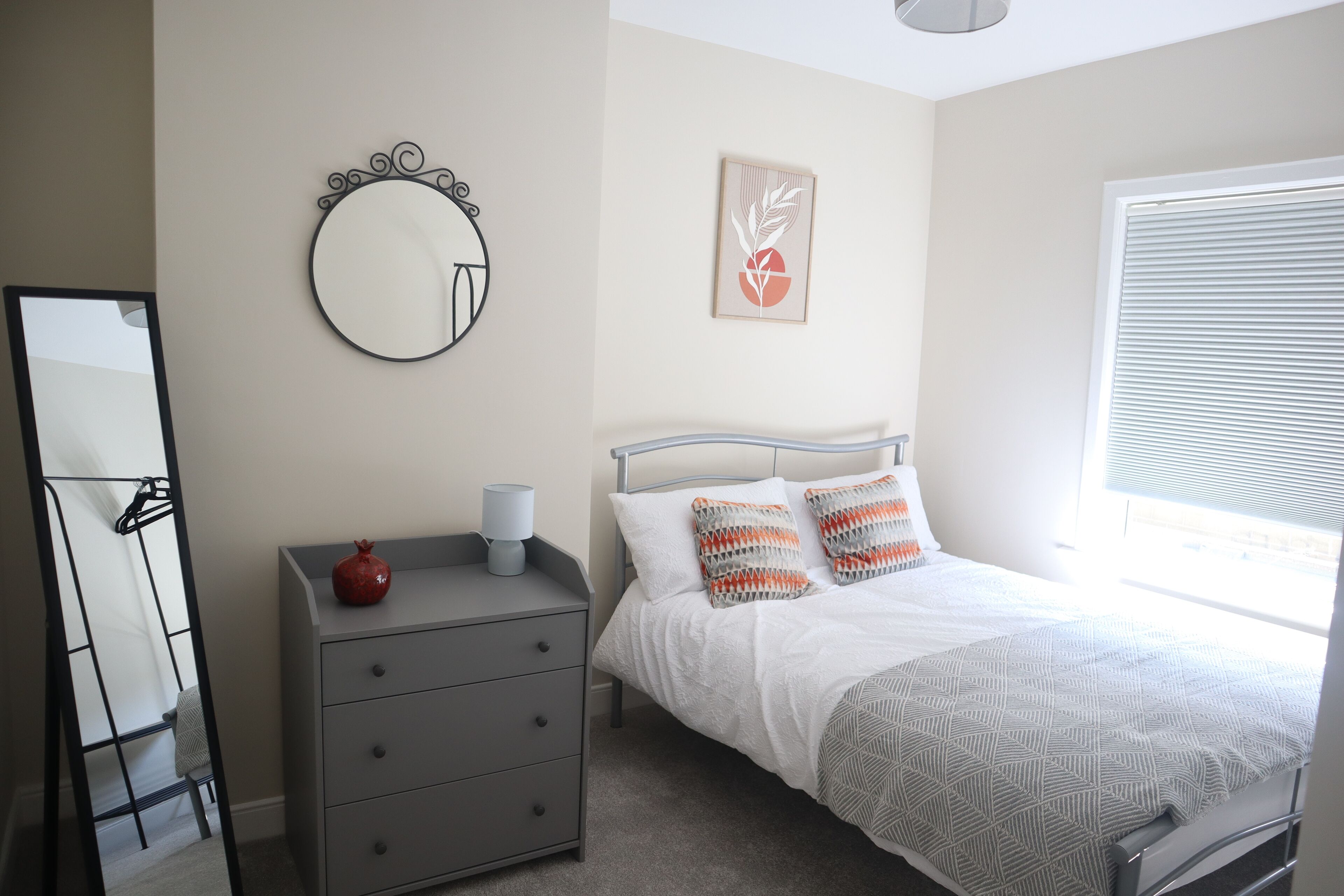 Une chambre à coucher comprenant un lit, une commode, un miroir et une œuvre d’art murale.