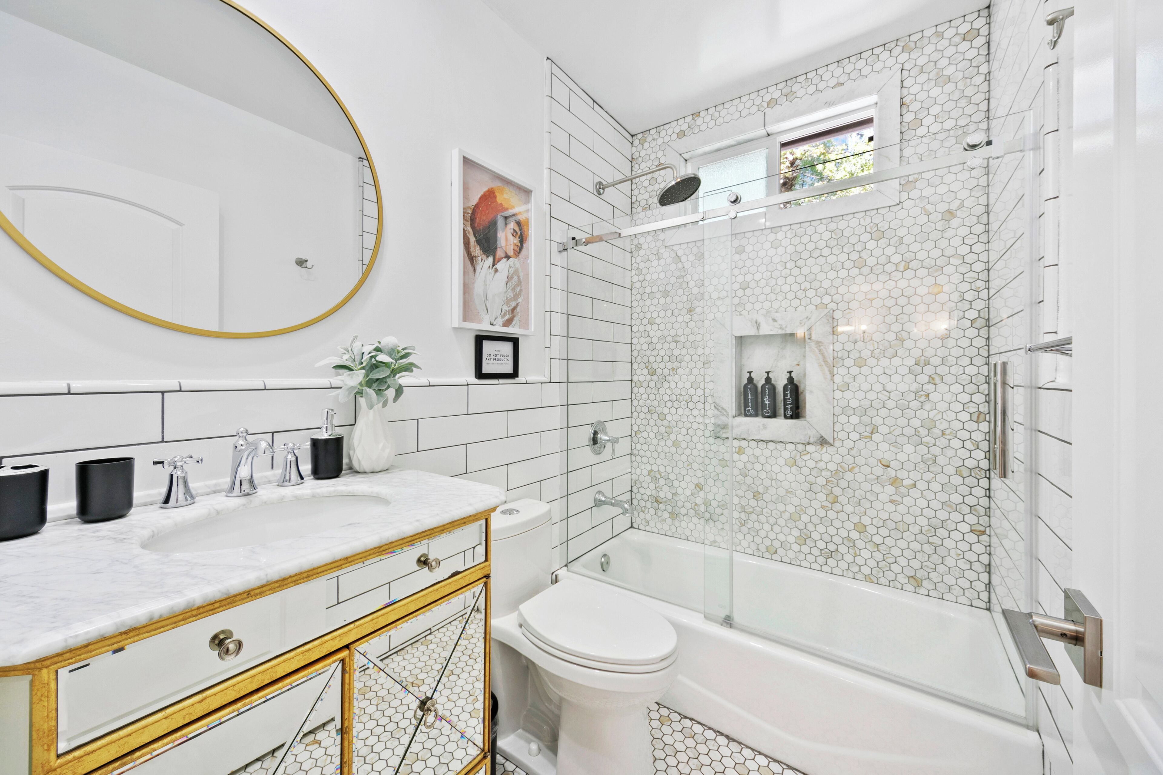 A bathroom with a white sink, gold-framed vanity, a toilet, and a glass-enclosed shower area with hexagonal tiles.