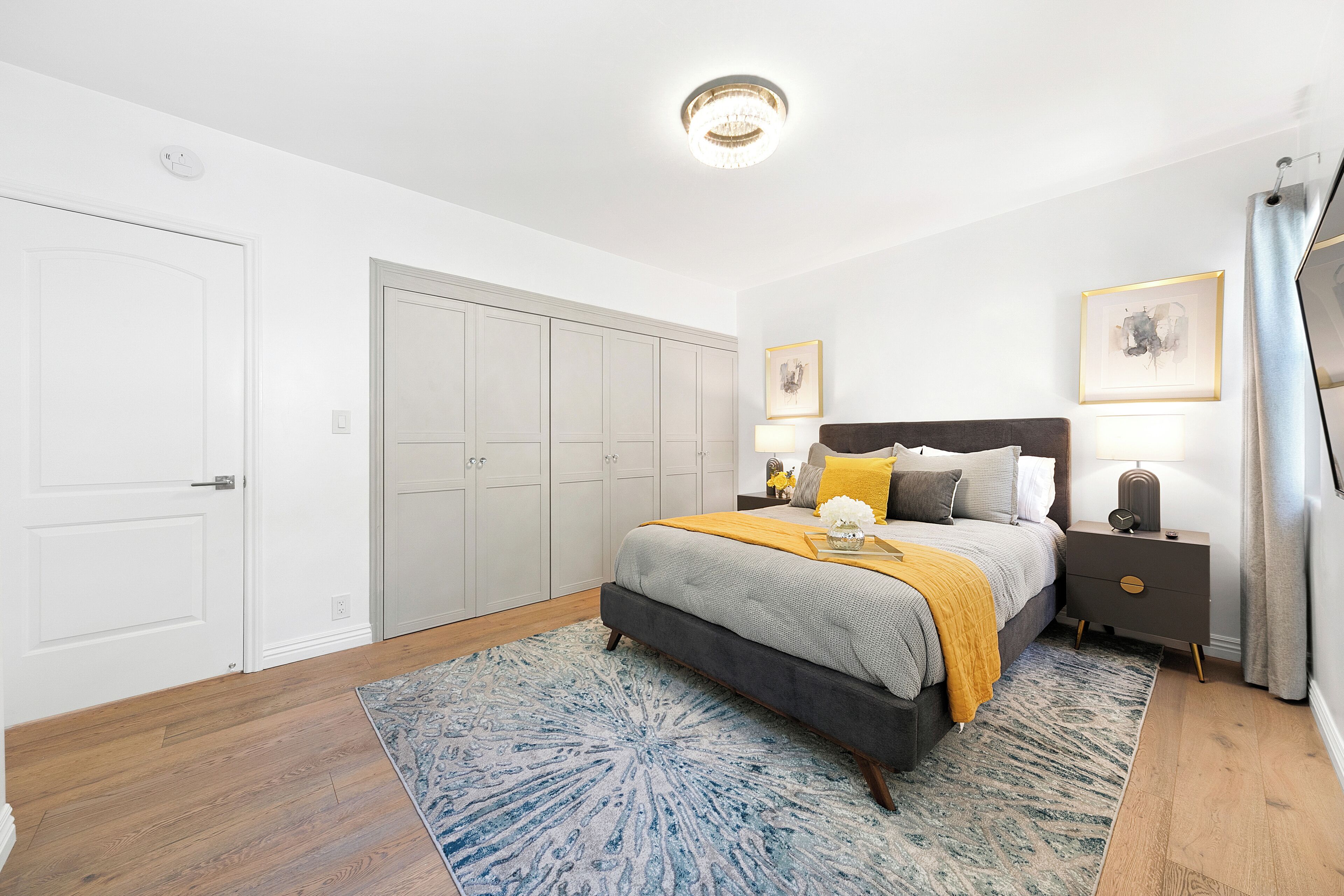 A bedroom with a bed, nightstands, a dresser, a wardrobe, and a chandelier.