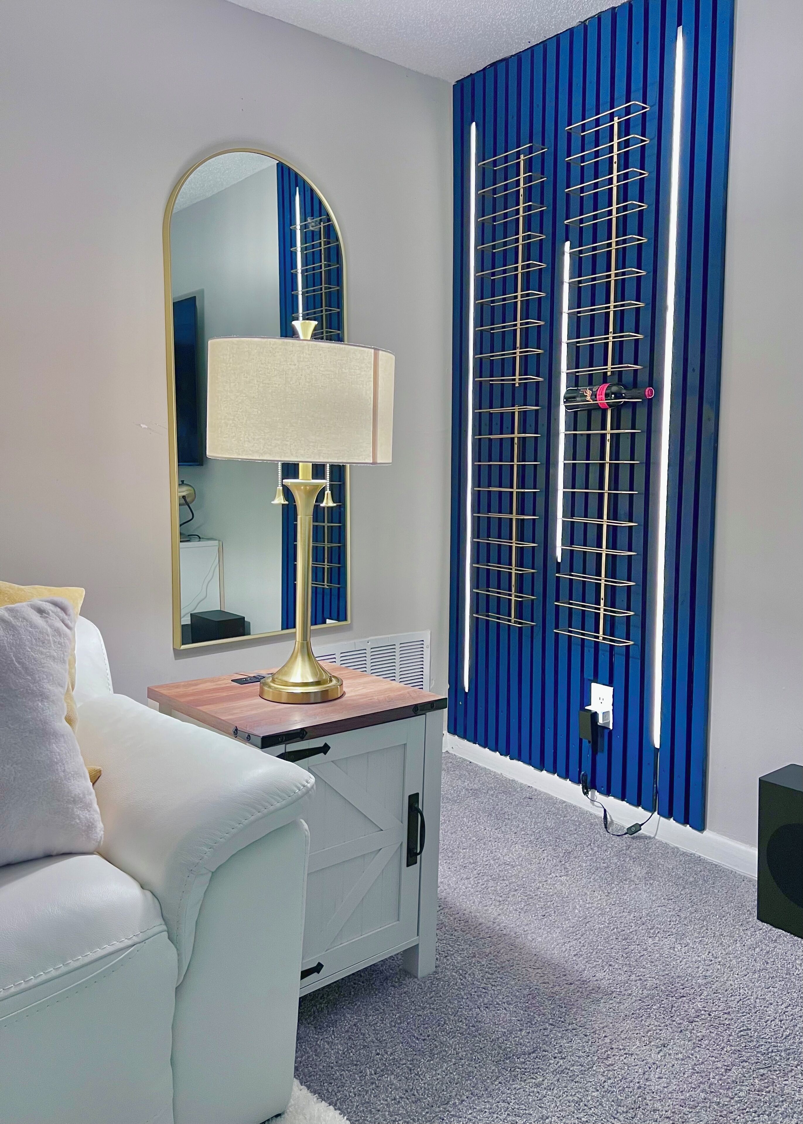 Een kamer met een witte bank, een lamp, een spiegel en een blauwe, gestreepte wand met een verticale plank.