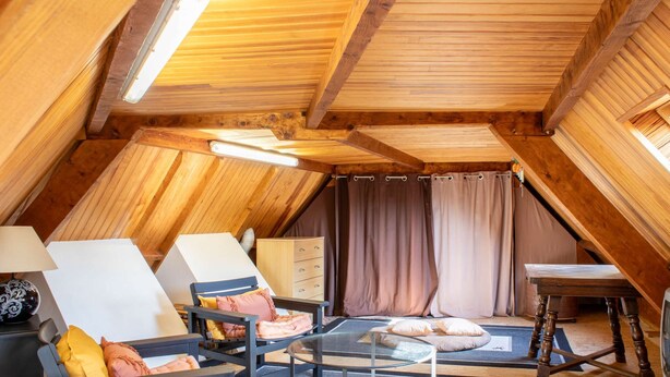 Una camera da letto mansardata accogliente, con soffitto spiovente, travi in legno, un letto con testiera, un tavolino e una sedia.