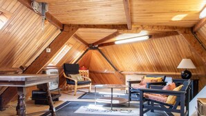 Una camera mansardata accogliente con soffitto in legno, un tavolo rotondo in vetro e un divano con cuscini.
