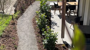 A pathway leading to a patio area with a table and chairs, surrounded by a garden with shrubs and a small tree. - Cozy Double Room - Private Entrance – Easy Self Check-In (Rum)
