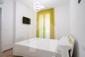 A hotel room with a bed, a television on the wall, and a window with yellow curtains.