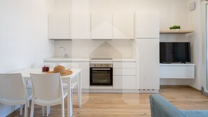Una cocina moderna con armarios blancos, horno empotrado y comedor con sillas blancas.