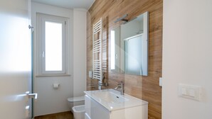 Un baño moderno con pared de madera, lavamanos blanco, espejo y retrete.