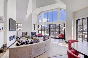 A spacious living area with a curved sofa, multiple chairs, and a large window offering a view of mountains. - Luxury 5BR Penthouse Residence at The Ritz-carlton Club Vail (Vail)