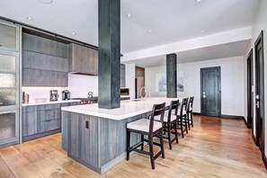 A modern kitchen with a central island, wooden cabinets, and a dining area with chairs. - Luxury 5BR Penthouse Residence at The Ritz-carlton Club Vail (Vail)