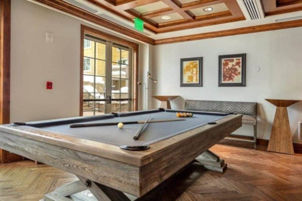 A pool table in a room with wooden flooring, a bench, and two framed artworks on the wall.