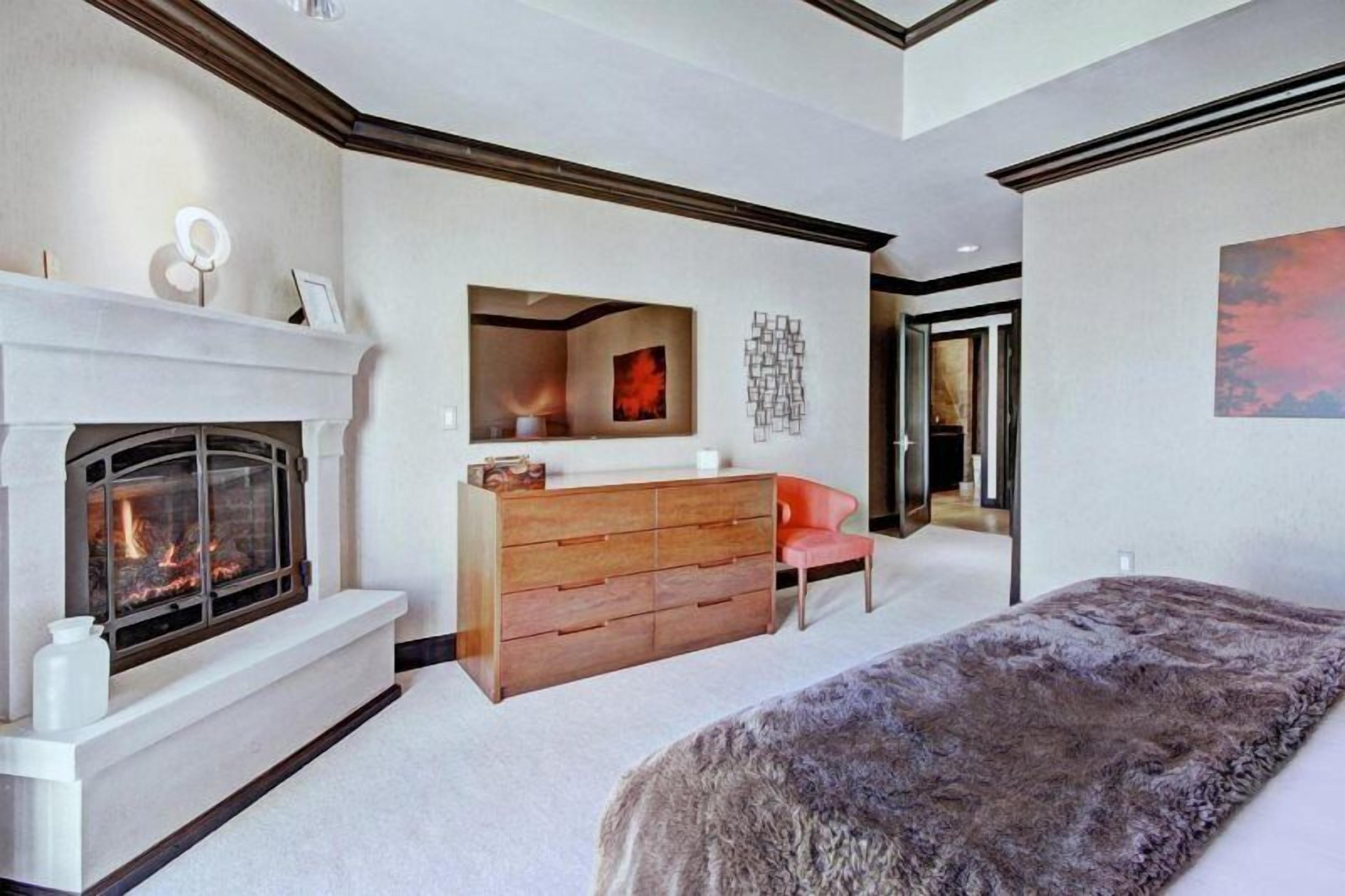 A bedroom with a fireplace, a dresser, a chair, and a large bed.