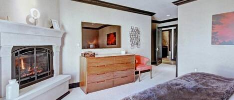 A bedroom with a fireplace, a dresser, a chair, and a large bed.