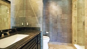 A bathroom with a black marble sink, a white toilet, and a shower area with stone tiles. - Luxury 5BR Penthouse Residence at The Ritz-carlton Club Vail (Vail)