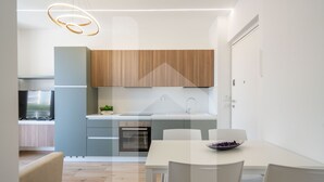 A modern kitchen with wooden cabinets, a built-in oven, and a white dining table with chairs. - Homiday - Residence Incanto - Mint (Alba Adriatica)