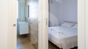 A modern bedroom with a wooden floor, a white bed, and a small bedside table. - Homiday - Residence Incanto - Mint (Alba Adriatica)