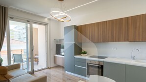 A modern kitchen with grey cabinets, a white countertop, and a stainless steel sink. There is a dining area with a white table and chairs, and a balcony with a view of buildings. - Homiday - Residence Incanto - Mint (Alba Adriatica)
