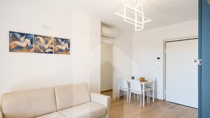 Ein modernes Wohnzimmer mit einem beigefarbenen Sofa, einem Esstisch mit Stühlen und einer weißen Tür.