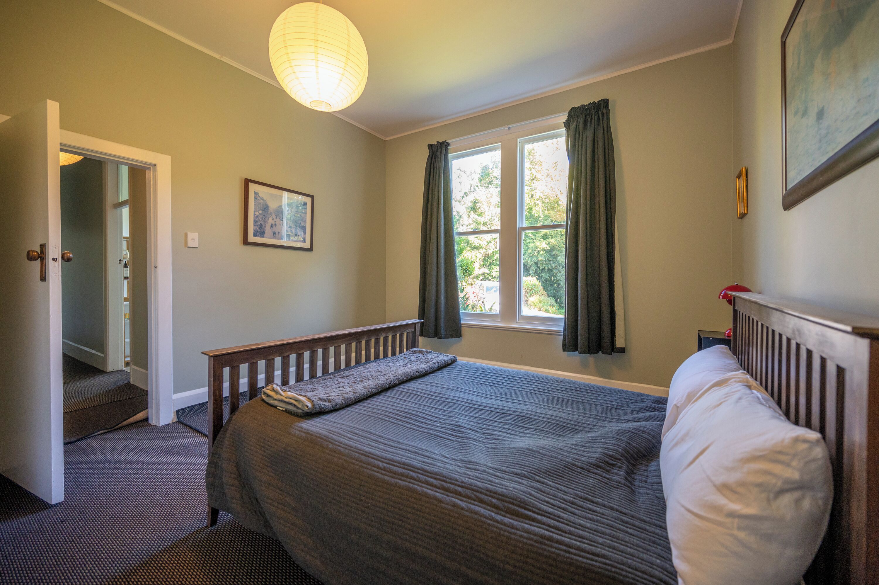 A bedroom with a bed, a window with curtains, a door, and a staircase leading to another room.