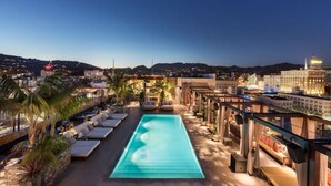Une piscine sur le toit, dotée de chaises longues et offrant une vue sur le paysage urbain au crépuscule.