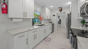 Una cocina moderna con armarios blancos, electrodomésticos de acero inoxidable y un extintor visible.