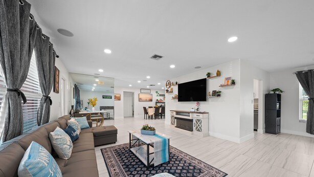 Una sala de estar moderna con un sofá, una mesa de centro y un televisor. Hay una zona de cocina con una mesa de comedor y sillas.