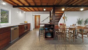 A kitchen with wooden cabinets, a dishwasher, and a dining area with a wooden table and chairs. - Cozy cabin in peaceful Wangoom with AC, WiFi (Wangoom)