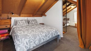A bedroom with a sloped ceiling, a bed with patterned bedding, a wooden dresser, and a small bedside table. - Cozy cabin in peaceful Wangoom with AC, WiFi (Wangoom)