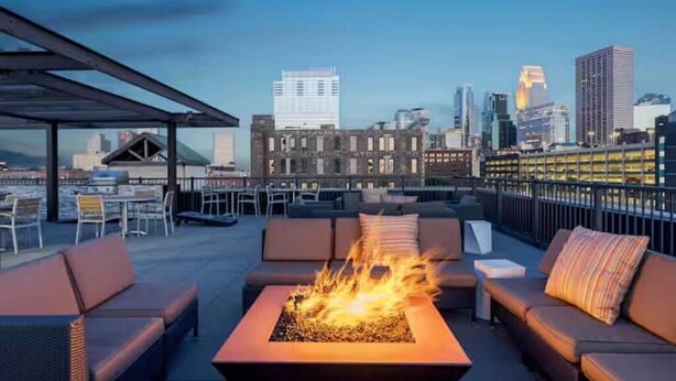 Eine Dachterrasse mit Feuerstelle, Sitzgelegenheiten und Blick auf den Stadt-Horizont.