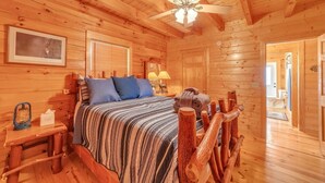 A wooden cabin bedroom with a bed, a nightstand, a lamp, and a ceiling fan. - Magic’s Rest 2 Bed Cabin located in Peaceful Gated Community with lake access (Lake Lure)