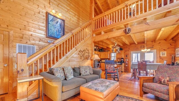 A wooden interior with a staircase, a sofa, a patterned ottoman, and a dining area. - Magic’s Rest 2 Bed Cabin located in Peaceful Gated Community with lake access (Lake Lure)
