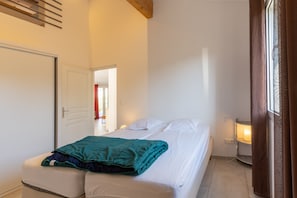 Une chambre à coucher avec un lit, une table de chevet avec une lampe, une porte et une fenêtre avec des rideaux.