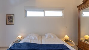 Ein Schlafzimmer mit einem Bett, zwei Nachttischlampen, einem Fenster, einem Spiegel und einem gerahmten Bild an der Wand.