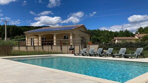 Ein Swimmingpool mit Liegestühlen, ein Gebäude mit einem Ziegeldach und ein Zaun.