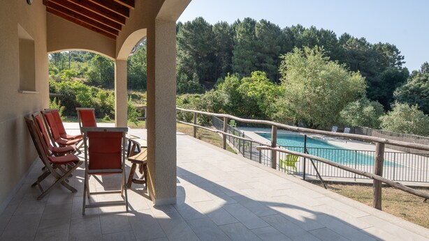 Ein überdachter Außenbereich mit Stühlen, einem Pool und Blick auf eine bewaldete Hügelkuppe.