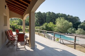 Un espace extérieur abrité, doté de chaises, d’une piscine et offrant une vue sur une colline boisée.