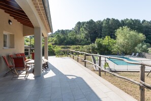 Un patio couvert avec des meubles d’extérieur, une piscine et une vue sur une zone boisée.