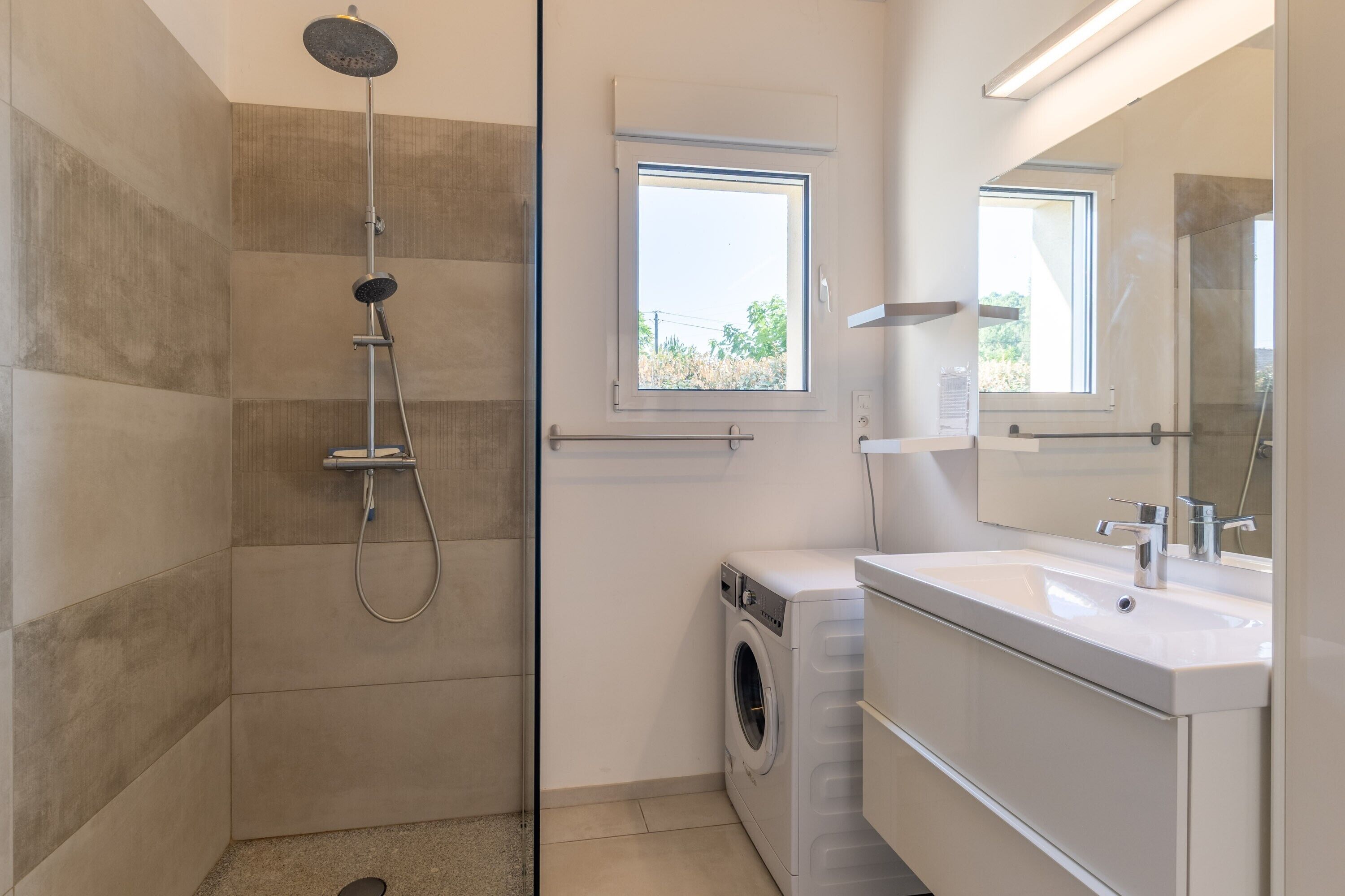 Un baño moderno con ducha, lavadora y lavabo con espejo.