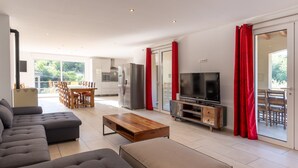 Ein modernes Wohnzimmer mit einer Couch, einem Holztisch, einem Fernseher und einer Küche im Hintergrund.