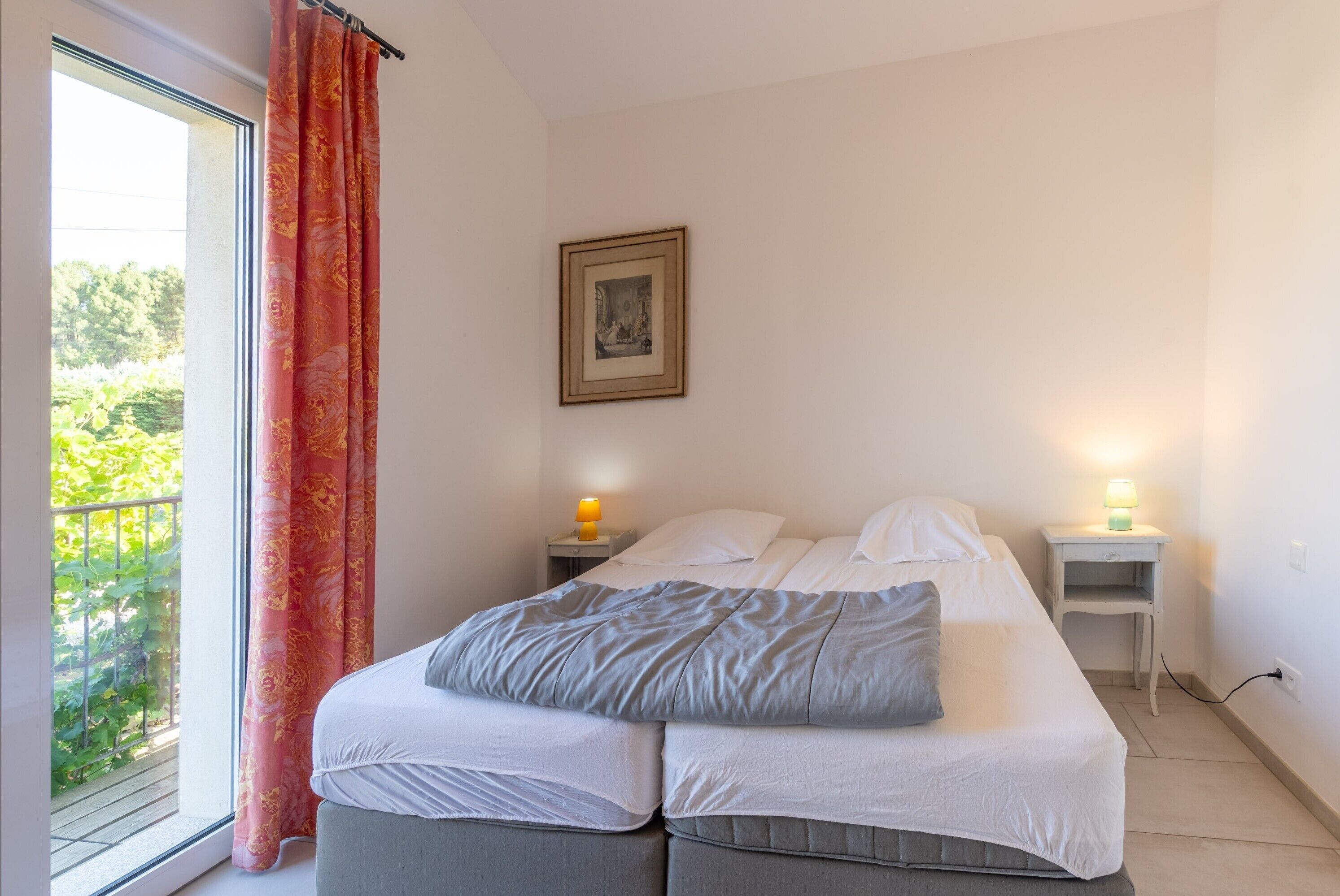 Een slaapkamer met een bed, twee nachtkastjes, een raam met gordijnen en een aan de muur hangend schilderij.