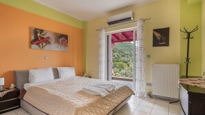 Un dormitorio con cama, mesita de noche, equipo de aire acondicionado, radiador, perchero y ventana con cortinas.
