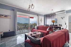 A modern living room with a red sofa, a coffee table, and a dining area with chairs and a table. - Apartment 'Spiri's House' with Private Terrace, Wi-Fi and Air Conditioning (Sívros)