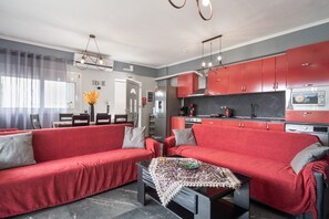 Una sala de estar moderna con sofás rojos, una mesa de centro con un objeto decorativo, y una cocina con armarios rojos y un microondas.