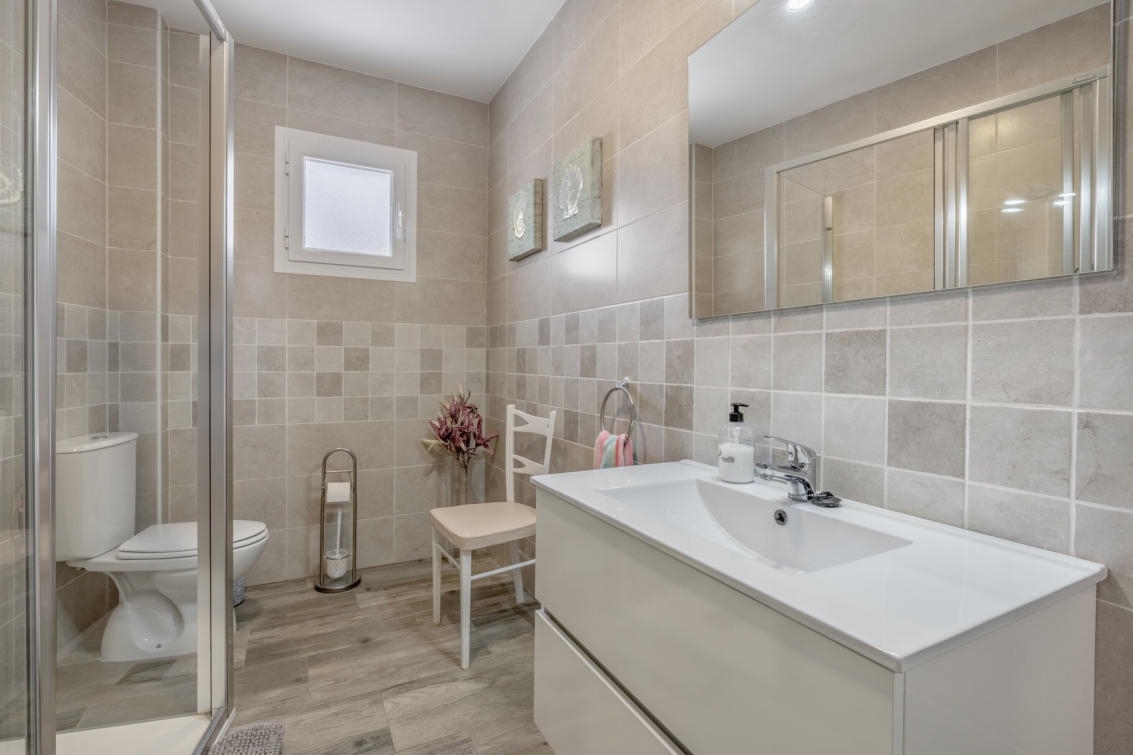 A modern bathroom with a glass shower enclosure, a white toilet, a vanity with a large sink, and a mirror.