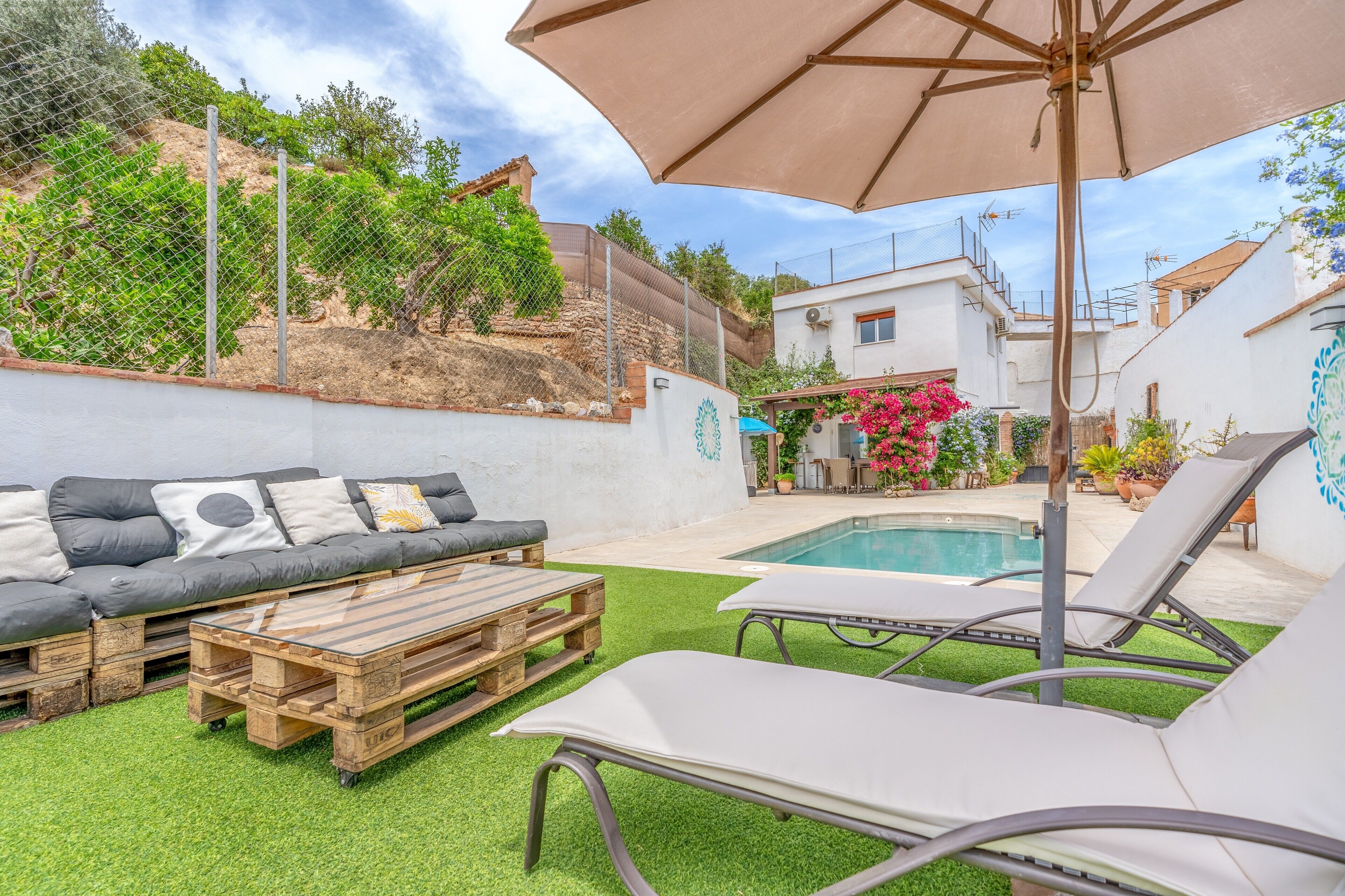 Un jardin avec une piscine, un canapé, des chaises longues et une table en bois.
