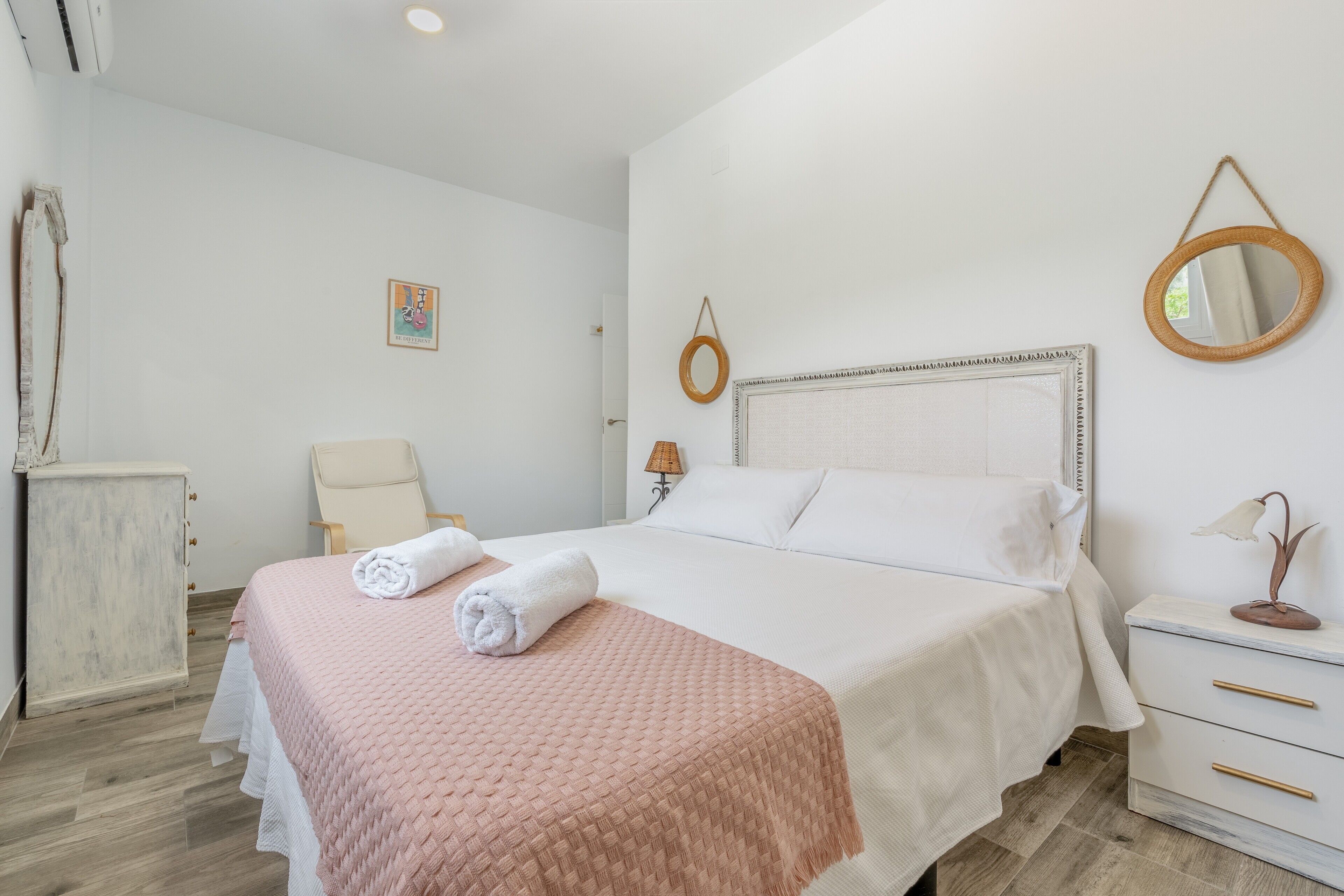 A neatly made bed with a pink blanket, a bedside lamp, and a small table with a flower vase.
