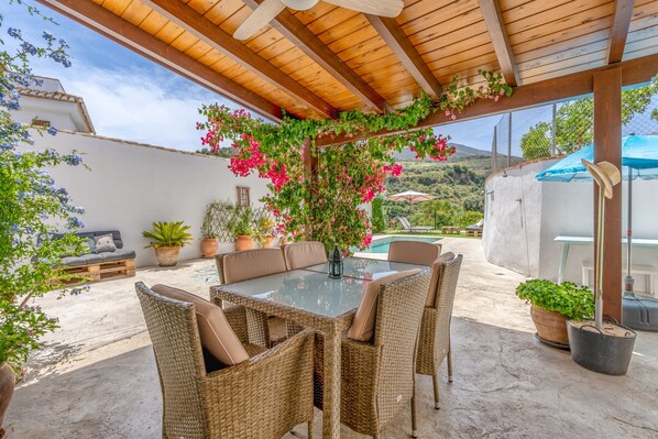 Un patio cubierto con mobiliario de mimbre, una mesa de vidrio y plantas en macetas.