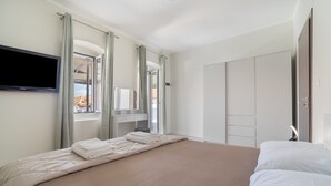 A hotel room with a bed, a TV mounted on the wall, a wardrobe, and a window with curtains. - Holiday Home 'Sparto' with Private Terrace, Wi-Fi and Air Conditioning (Spartochori)