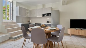 A modern kitchen with grey cabinets, a dining area with a round table and chairs, a TV, and a staircase leading to an outdoor area. - Holiday Home 'Sparto' with Private Terrace, Wi-Fi and Air Conditioning (Spartochori)